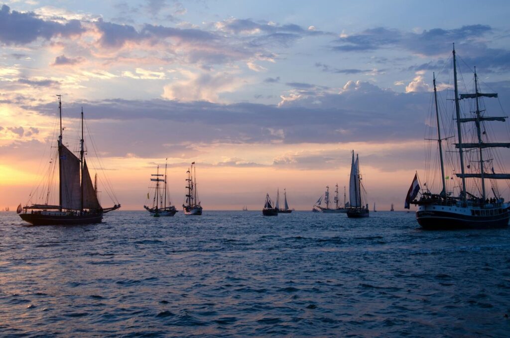 A fleet of classic sailing ships on the open sea during a stunning sunset, offering a serene maritime scene.